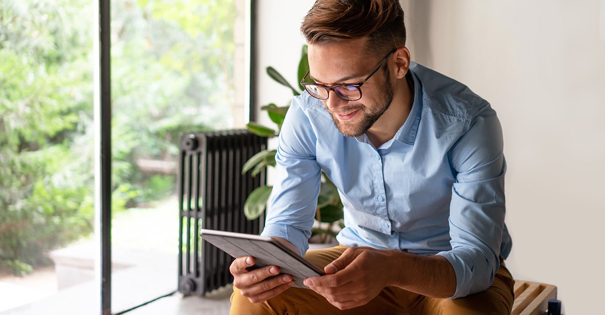 Ein Mann mit Brille sitzt auf einer Bank und nutzt ein Tablet.